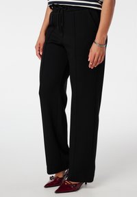 Zwarte wijde broek gemaakt van een zachte stof met een trekkoord in de taille en zijnaad. Gecombineerd met puntige rode hoge hakken.
