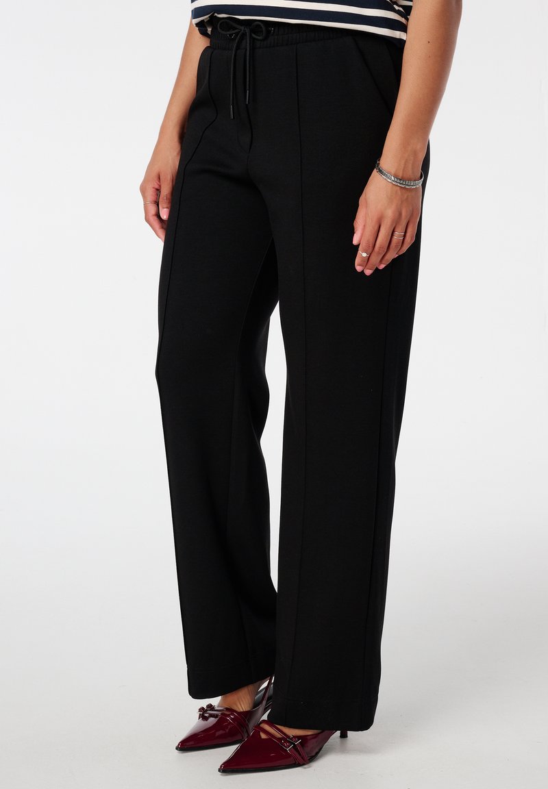 Zwarte wijde broek gemaakt van een zachte stof met een trekkoord in de taille en zijnaad. Gecombineerd met puntige rode hoge hakken.