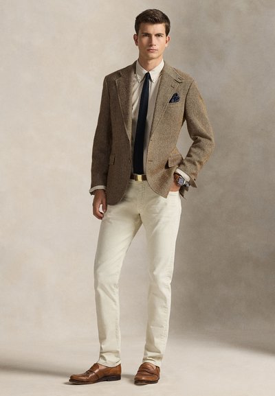 Καφέ σακάκι με σχέδιο ψαροκόκαλο πάνω σε πουκάμισο με ρίγες, συνδυασμένο με κρεμ παντελόνια και καφέ loafers, με έμφαση σε σκούρο γραβάτα και μαντηλάκι τσέπης.