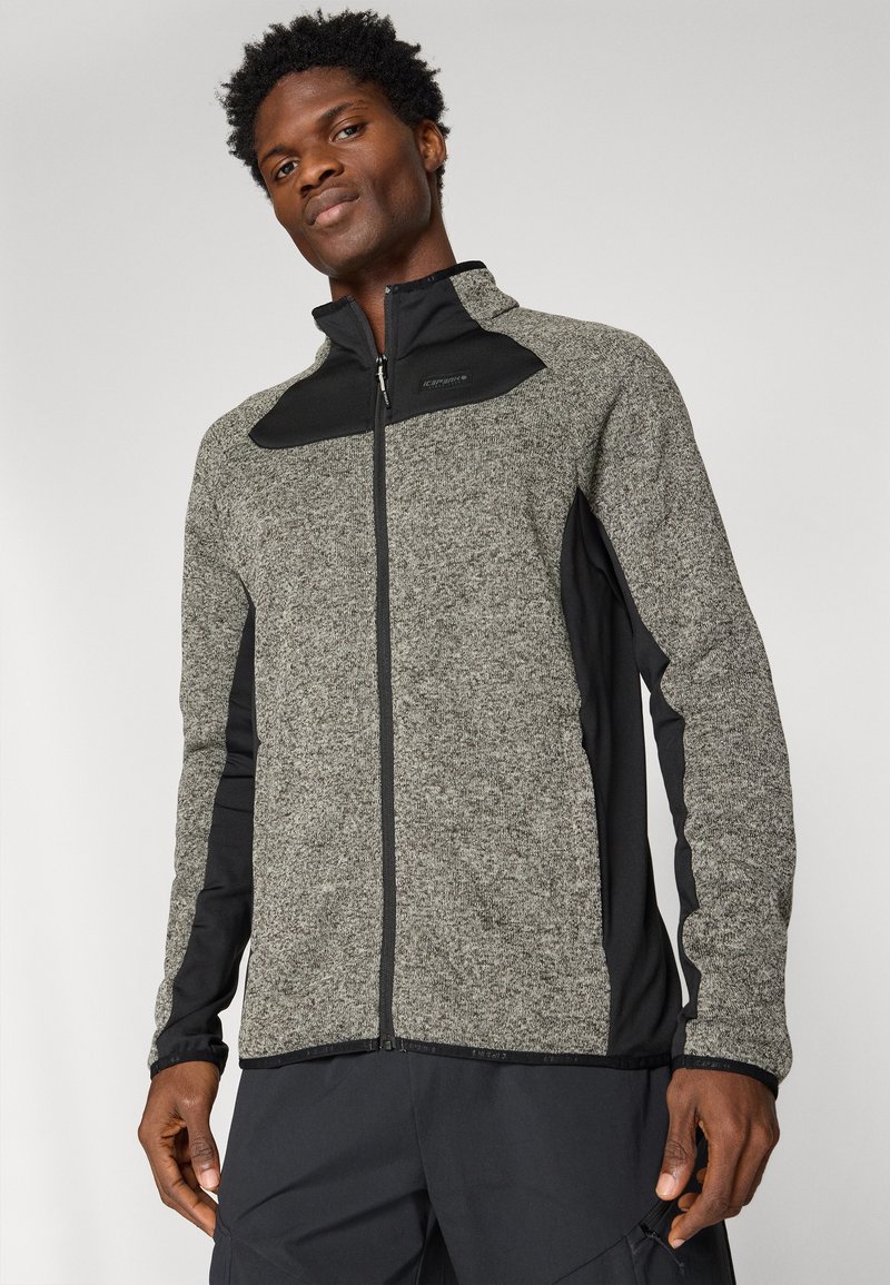 Szara polarowa kurtka z czarnymi akcentami, wysoki kołnierz, zamek błyskawiczny z przodu i kieszenie boczne. Teksturowany materiał z gładkimi, kontrastującymi rękawami.