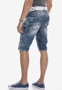 Lichtblauwe denim cargo shorts met meerdere zakken en een vervaagde structuur. Gedragen met een witte riem en blauwe sneakers.
