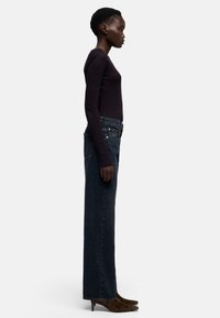 Donkerpaars top met lange mouwen, gecombineerd met hooggesneden recht gesneden donkere spijkerbroeken en bruine schoenen met spitse neus, zijaanzicht.