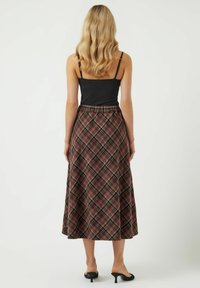 Gonna maxi a quadri in tonalità di marrone, con una vita arricciata e un design fluido, abbinata a un top aderente nero e mule con tacco.