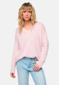 Pull en V léger rose, surdimensionné, avec des manches longues, fabriqué dans un tissu doux et texturé, associé à un jean taille haute bleu clair.