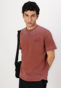 Tricou roșu din bumbac, cu mâneci scurte, guler rotund și un mic logo pe piept. Prezintă o textura estompată și cusături contrastante.