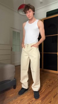 White tank top, cream-colored wide-leg pants with front pockets, light wood floors in background, and dark shoes. Simple, casual outfit.