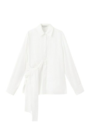 Camisa blanca de manga larga con botones, cuello puntiagudo y detalle de lazo asimétrico de tela en el lado izquierdo.