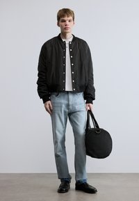 Μαύρο μπουφάν bomber με ασημένια κουμπιά, λευκό t-shirt, ανοιχτόχρωμο μπλε τζιν και μαύρη στρογγυλή τσάντα ώμου. Φοράει μαύρα παπούτσια.