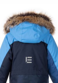 Niebieska i granatowa wodoodporna kurtka z kapturem wyłożonym sztucznym futrem i logo z tyłu. Główny materiał wydaje się gładki i bez faktury.