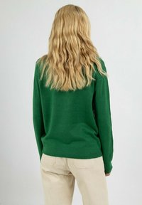 Pull en tricot vert avec un col rond et des manches longues, vu de dos, associé à un pantalon beige clair. Texture lisse.