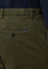 Olijf groene broek met een gladde textuur, voorzien van een knoopsluiting, gestikte tailleband en een klein blauw "HACKETT" label op de achterzak.