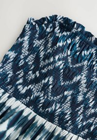 Blå och vit tie-dye klänning med smockad byst, volangkrage och svävande kjol, med en mjuk textur och lager på lager-mönster.