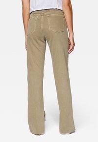 Vista posteriore di una persona che indossa pantaloni beige a vestibilità ampia con tasche posteriori, orli sfrangiati e una camicia bianca infilata dentro.