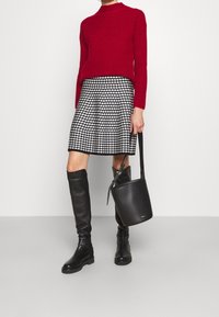 Punainen ribbineulottu neulepusero, mustavalkoinen koiranhampaakuvioinen hame, polveen ulottuvat mustat nahkasaappaat ja pyöreä musta olkalaukku nauhalla.