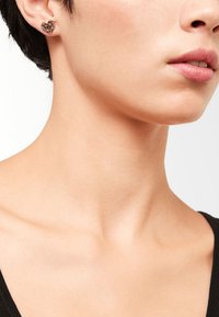 Orecchini geometrici in metallo a forma di cuore, caratterizzati da una finitura metallica lucida con un motivo simile a diamanti, indossati sull'orecchio di un modello.