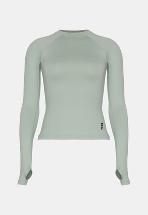 Vartaloa myötäilevä pitkähihainen vaaleanvihreä urheilupaita peukaloaukkoineen ja pienellä mustalla logolla alaoikealla.