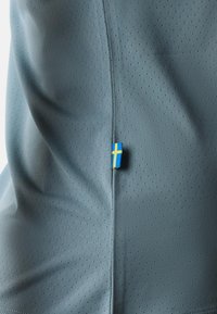 Hellblau perforierter Stoff mit einem kleinen eingenähten Etikett, das die schwedische Flagge in Gelb und Blau nahe einer Naht zeigt.