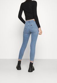 Jeans ajustados de denim azul claro con una cintura alta, con bolsillos traseros y un ligero estiramiento. Combinados con botas negras hasta el tobillo.