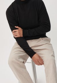Pull à col roulé noir avec des manches longues, associé à un pantalon en velours côtelé beige clair à rayures verticales. Texture lisse, coupe décontractée.