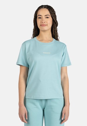 Hellblaues T-Shirt mit kurzen Ärmeln aus weichem Material, das einen runden Ausschnitt und ein kleines Logo auf der Brust hat. Locker geschnitten.