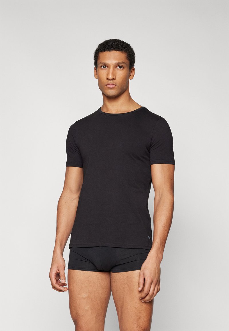 T-shirt noir à manches courtes en tissu doux. Doté d'un col rond classique et d'une coupe ajustée. Porté avec un shorty noir.