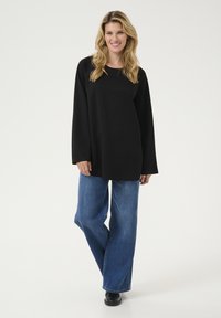 Top negru cu maneci lungi, cu guler rotund, asociat cu pantaloni largi din denim albastru. Ținuta prezintă linii simple și curate.