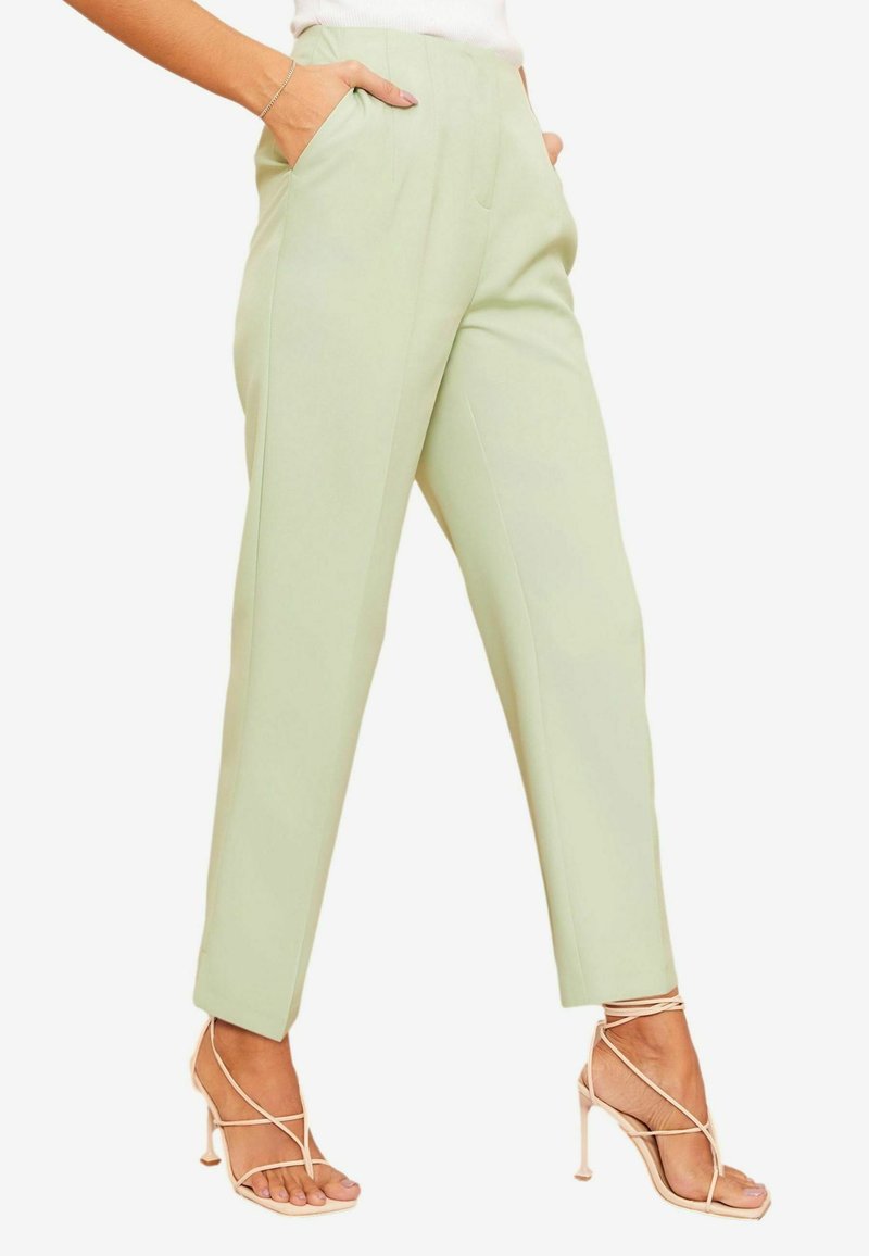Pantaloni su misura verde chiaro con due tasche laterali e vestibilità slim. Tessuto liscio con una piega sul davanti, abbinati a tacchi nude con cinturini.