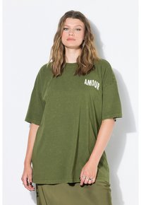 Olivově zelené oversized tričko vyrobené z měkké tkaniny má krátké rukávy a na levé straně nápis "AMOUR" bílou barvou.