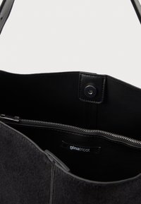 Fekete filcből készült bevásárlótáska cipzáros rekesszel, patent záródással, sima felülettel, és egy belső címkével, amelyen a "ginatricot" felirat olvasható.