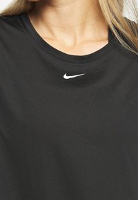 Mujer vistiendo una camiseta Nike negra con un pequeño logotipo de swoosh blanco debajo del escote.