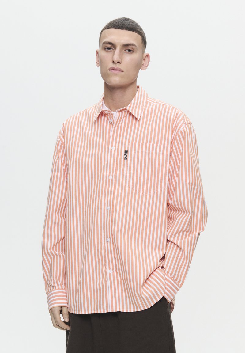 Chemise rayée orange et blanche avec une coupe décontractée, dotée d'un devant à boutons, d'un col, d'une poche poitrine unique et d'un détail de logo.