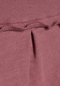 Jasnoróżowy materiał z ryżowym splotem. Posiada delikatną falbanę wzdłuż górnej krawędzi oraz małe pionowe rozcięcie na środku.