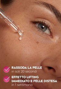 Droplet di siero trasparente vengono applicati su una pelle liscia, mostrando il riflesso della luce sulla texture della pelle e la forma della pipetta di vetro.