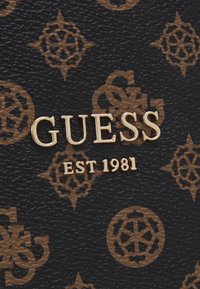 Czarny materiał teksturowany z wytłoczonymi brązowymi wzorami. Zawiera złote logo „GUESS” oraz napis „EST 1981”. Trwały i stylowy design.