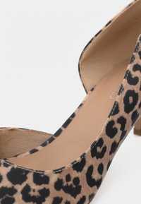 Γυναικείο παπούτσι με ψηλό τακούνι και λεοπάρ μοτίβο, με στρογγυλεμένη μύτη, λεία υφή και χαμηλό χοντρό τακούνι σε ουδέτερη χρωματική παλέτα.