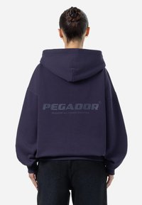 Felpa oversize blu navy con un ampio cappuccio, maniche a palloncino e un logo stampato sul retro. Realizzata in morbido tessuto testurizzato.