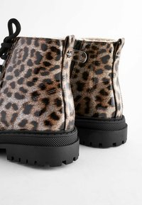 Botas de tobillo con estampado de leopardo y acabado brillante, suela texturizada negra y forro de piel. Incluye cordones negros y acentos de hardware en forma de estrella.