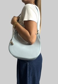 Jasnoniebieska skórzana torebka o zaokrąglonym kształcie z bocznym paskiem, z metalowymi elementami w kolorze srebrnym i gładką teksturą.