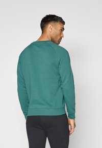 Tegroen sweatshirt met een ronde hals en geribde manchetten. Gladde textuur, aansluitend ontwerp en een rechte zoom, gecombineerd met zwarte broek.