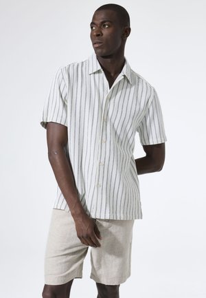 Kurzärmeliges, gestreiftes Hemd, weiß mit dunkelblauen vertikalen Linien, vorne mit Knöpfen. Kombiniert mit beigen Leinen-Shorts, glatte Textur, lockere Passform.