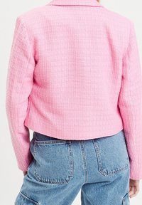 Blazer texturé rose avec un design raccourci et un col cranté, associé à un jean bleu taille haute avec des poches arrière.