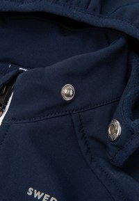 Navy blue jacket fabric with silver snap buttons and contrasting white stitching. Features a soft inner lining and a structured collar.