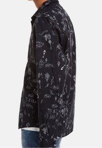 Camisa negra con un patrón gráfico que incluye ilustraciones blancas, palabras y símbolos. Mangas largas y cuello puntiagudo. Material de algodón.