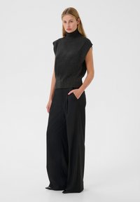 Melna bez piedurknēm turtleneck blūze ar teksturētu adījumu, apvienota ar platām melnām biksēm ar sānu kabatām. Gluda, plūstoša auduma.