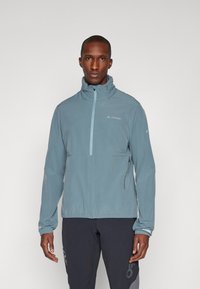 Veste légère bleue avec col montant, fermeture éclair mi-hauteur et poignets élastiques. Présente un branding subtil sur la poitrine et une poche latérale zippée.