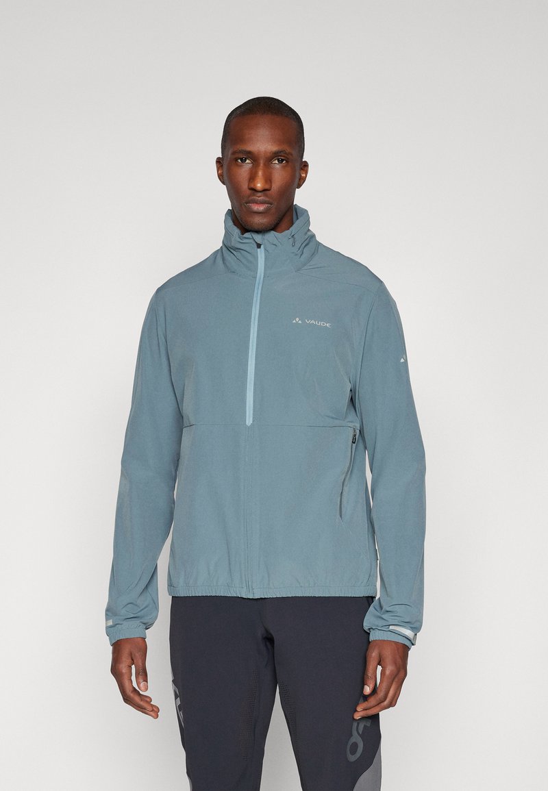 Veste légère bleue avec col montant, fermeture éclair mi-hauteur et poignets élastiques. Présente un branding subtil sur la poitrine et une poche latérale zippée.