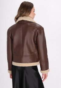 Brun læderjakke med en krave og manchetter i cremefarvet faux shearling. Designet har en cropped længde og en glat tekstur.