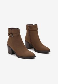 Bottines en suède marron avec un bout arrondi, un talon bloc de hauteur intermédiaire, un détail de boucle et une fermeture éclair sur le côté pour un enfilage facile.