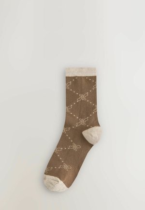 Braune Socke mit einem gemusterten Design in Creme, das Wirbel und gepunktete Linien zeigt. Heller beigefarbener Abschluss und Zehenbereich, weicher Stofftextur.