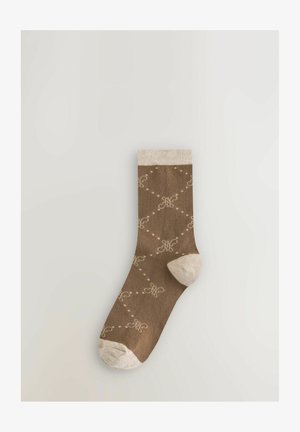 Braune Socke mit einem gemusterten Design in Creme, das Wirbel und gepunktete Linien zeigt. Heller beigefarbener Abschluss und Zehenbereich, weicher Stofftextur.